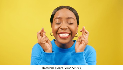 Beautiful young woman with fingers crossed, wishing and hoping, yellow studio - Shutterstock ID 2364727711