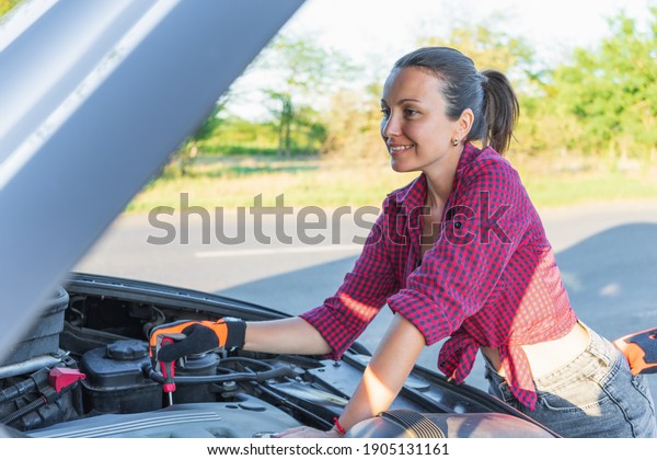 Beautiful young woman\
fixing the car on the roadside . Girl in shirt and jeans ready to\
repairing her car. woman mechanic . broken car on the road and\
woman waiting for\
help