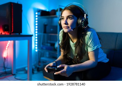 Beautiful young woman focusing on winning a video game with a remote controller. Female gamer enjoying a video game in a console during a leisure day in her bedroom - Powered by Shutterstock