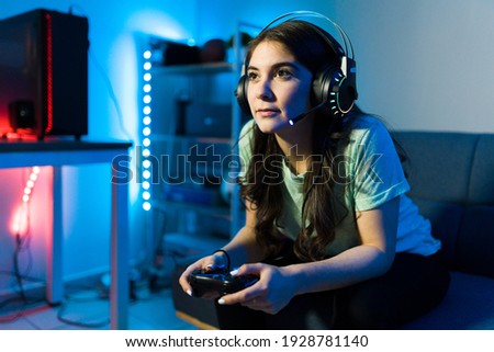 Beautiful young woman focusing on winning a video game with a remote controller. Female gamer enjoying a video game in a console during a leisure day in her bedroom