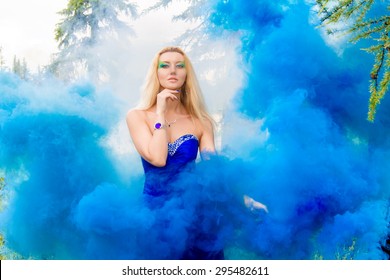 Beautiful Young Woman In Forest In Cloud Of A Bright Blue Smoke