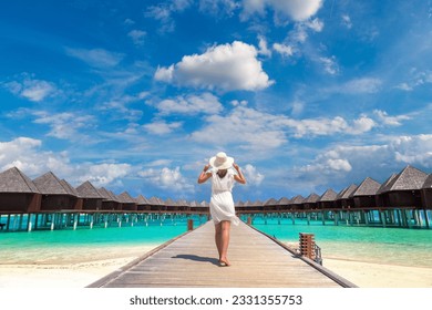 Beautiful young woman in front of water luxury villas standing on the tropical beach jetty (wooden pier) in Maldives island