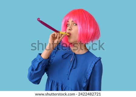 Beautiful young woman in funny disguise with party whistle on blue background. April Fools Day celebration