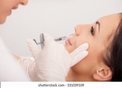 Beautiful young woman is getting botox injection in her face. The expert beautician is holding syringe and filling liquid carefully