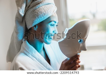 Beautiful young woman getting a led light therapy mask treatment  for her face at the beauty salon.