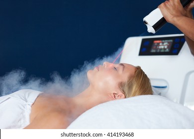 Beautiful young woman getting local cryotherapy therapy in cosmetology clinic. Beautician applying cold nitrogen vapors to the face of woman.
