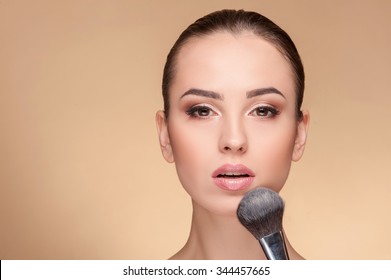 Beautiful young woman is getting make-up. She is sitting and looking at camera with passion. The beautician is applying a powder on her chin. Isolated and copy space in left side