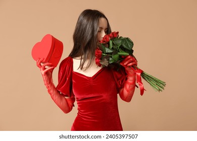 Beautiful young woman with gift box in shape of heart and bouquet of red roses on brown background. Valentine's Day celebration