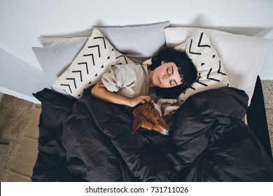 Beautiful Young Woman Or Girl Cuddles And Hugs Her Best Friend Basenji Puppy Dog, Sleep Together Under Blankets In Hipster Designer Bed On Cold Day, Peace And Quiet