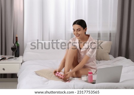 Beautiful young woman giving herself pedicure on bed at home