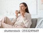 Beautiful young woman with glass cup of hot cocoa sitting on sofa in living room