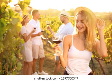 Beautiful young woman with glass of wine and her friends in vineyard on sunny day - Powered by Shutterstock