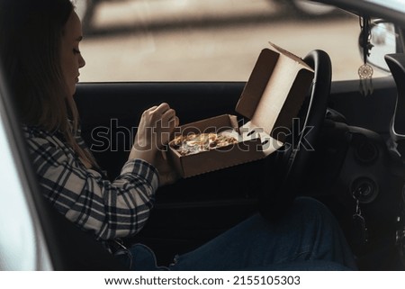 a beautiful young woman is going to have lunch in her car, in her hands she has a box with ready-made appetizing pizza