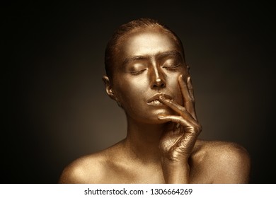 Beautiful young woman with golden paint on her body against dark background