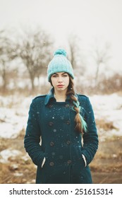 Beautiful Young Woman In Green Coat And Mint Beanie Hat And Dyed Hair Outdoors In Winter. Hipster Teenage Girl In Snow Standing Looking At Camera. Retouched, Filter, Vertical, Matte Finish Edit.