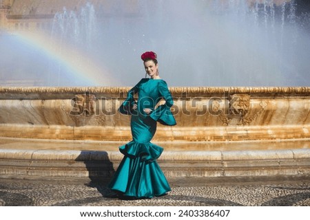 Beautiful young woman in a green frilly suit with a flower on her head. The woman is dancing flamenco and is in the most famous square in seville, spain, in front of its central fountain