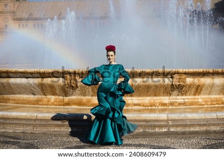 Beautiful young woman in a green frilly suit with a flower on her head. The woman is dancing flamenco and is in the most famous square in seville, spain, in front of its central fountain