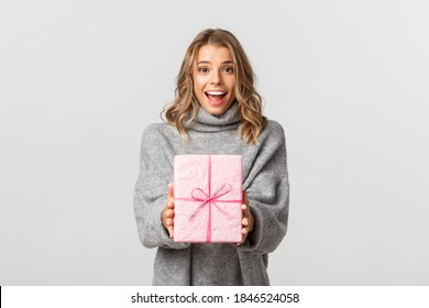 Beautiful Young Woman In Grey Sweater, Giving Gift, Congratulating Someone With Birthday, Standing Over White Background