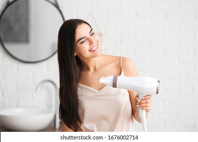 Hermosa joven mujer con secador de pelo en el baño
