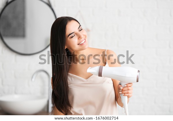 Beautiful young\
woman with hair dryer in\
bathroom