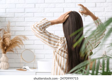 Beautiful young woman with hair spray sitting at home, back view - Powered by Shutterstock