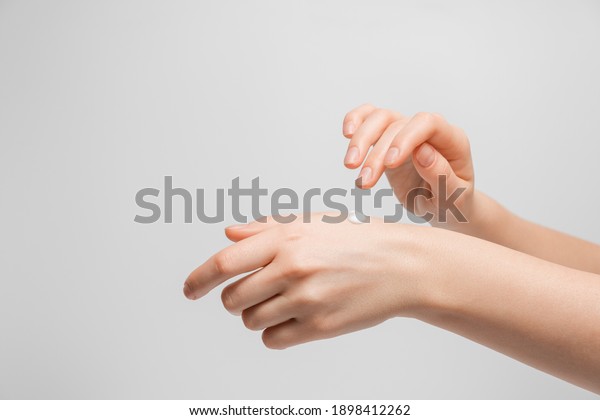 Beautiful young woman hands with cream.\
Woman applies cream on her hands on grey background. Palms down\
with smooth skin on hands, nice natural short\
nails.