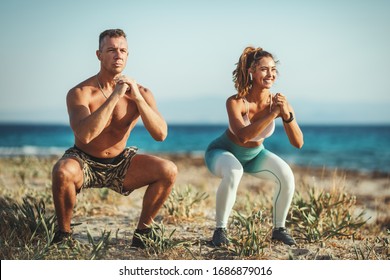 A Beautiful Young Woman And Handsome Man Are Doing Stretching Exercise At The Sea Beach In Summer Sunny Day.