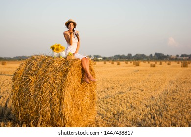 Beautiful Young Woman In A Hat In A Sundress Sits On A Haystack Straw Summer August Nature