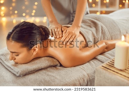 Beautiful young woman having back massage in spa salon. Serene relaxed woman lying on couch with closed eyes receiving relaxing massage. Beauty treatment, body care