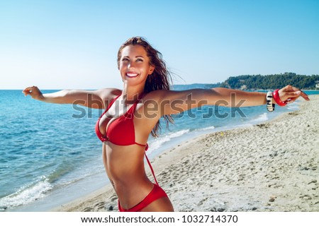 Beautiful young woman having fun on the beach. She is standing with open arms and pensive looking away with smile on her face. 