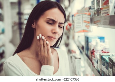 Beautiful Young Woman Is Having A Toothache While Choosing A Remedy At The Pharmacy