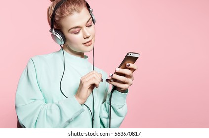 Beautiful young woman in headphones listening to music smiling with closed eyes standing on a pink background in a blue sweatshirt - Shutterstock ID 563670817
