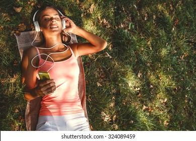 Beautiful young woman with headphones lying on grass and listening to music