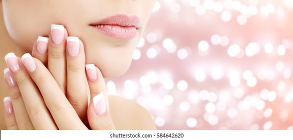Beautiful young woman with healthy skin and french manicure on an abstract background with blurred lights