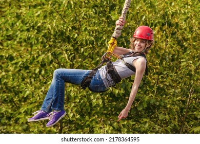 Beautiful Young Woman In A Helmet Hanging On A Rope After The Bungee Jump Against Green Foliage