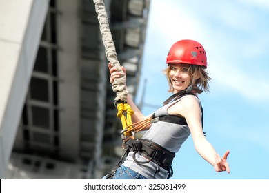 Beautiful Young Woman In A Helmet Hanging On A Rope After The Bungee Jump Against The Sky