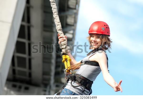 beautiful young woman in a helmet hanging\
on a rope after the bungee jump against the\
sky