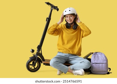 Beautiful young woman in helmet with modern electric kick scooter sitting against yellow background - Powered by Shutterstock