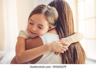 Beautiful young woman and her charming little daughter are hugging and smiling