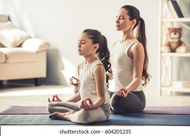 Hermosa joven y su encantadora hija pequeña están sonriendo mientras hacen yoga juntas en casa Foto de stock