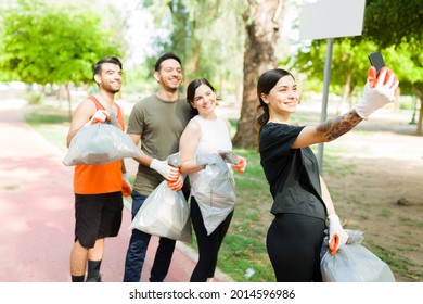 Beautiful Young Woman And Her Group Of Diverse Friends Taking A Selfie With Her Smartphone After Running While Picking Up Trash Outdoors