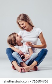 Beautiful Young Woman With Her Little Cute Daughter Are Sitting On White Background. Mom With Daughter Isolated. Tenderness