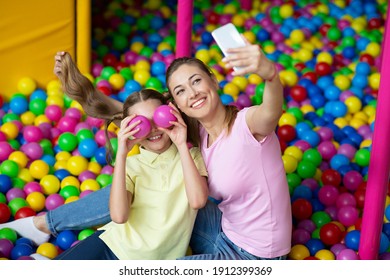 Beautiful Young Woman With Her Teen Daughter Taking Selfie Together At Ball Pond In Kids Amusement Centre. Happy Parent And Adolescent Child Making Photo Of Themselves On Playground