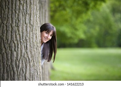 Beautiful Young Woman Hiding Behind A Tree