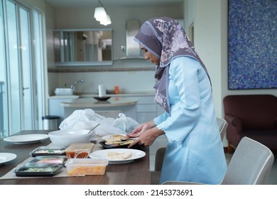 A Beautiful Young Woman In Hijab Puts Traditional Malay Food On The Dining Table And Prepares For The Eid Mubarak Celebration In The Dining Room.