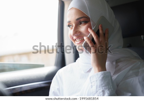 Beautiful young woman in hijab sitting in a car and\
talking on the phone