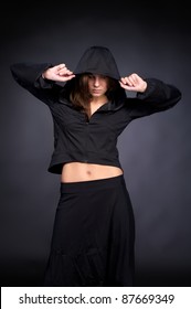 Beautiful young woman in hip hop style with hood on the head against black wall
