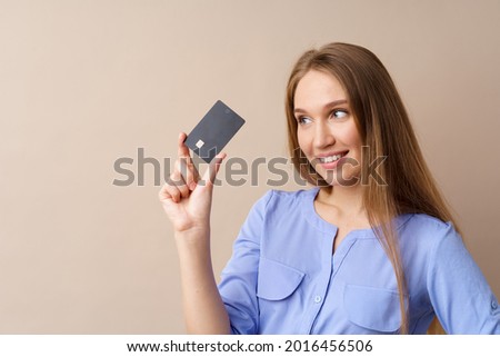 Beautiful young woman holding black credit card against beige background