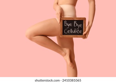 Beautiful young woman holding board with text BYE BYE CELLULITE on pink background