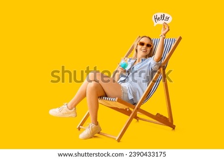 Beautiful young woman holding cocktail and paper speech bubble with word HELLO on yellow background